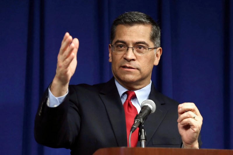 Attorney general Xavier Becerra standing at microphone speaking and gesturing with hand