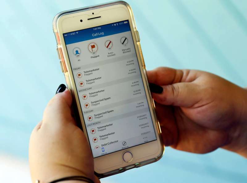 A woman holds an iPhone that shows a list of spam calls