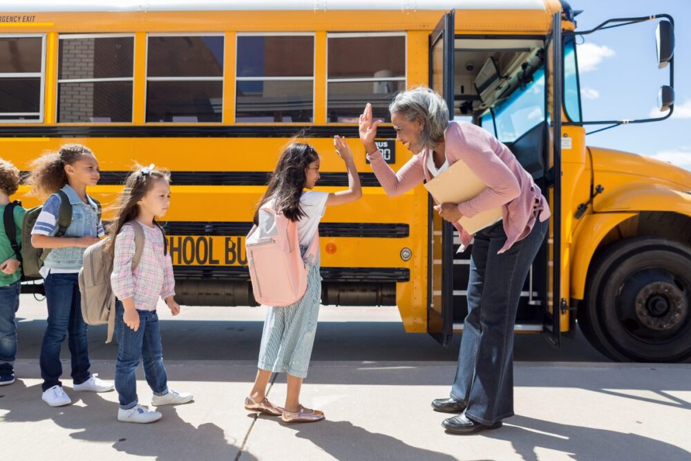 Public school support staff deserve a living wage. Photo of support staff and students in front of bus.