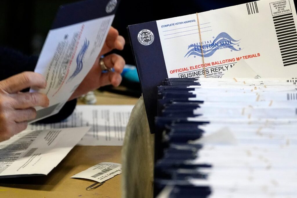 Image of several mail in ballots on the right. Hands holding mail in ballots on left.