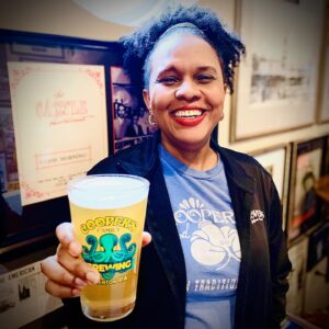 A woman in a Cooper's Seafood House shirt holding a Cooper's Seafood House pint of frothy beer.