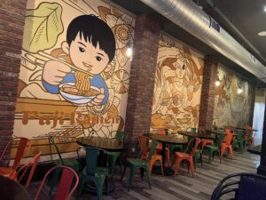A mural with cartoon depictions of people eating ramen inside a restaurant.