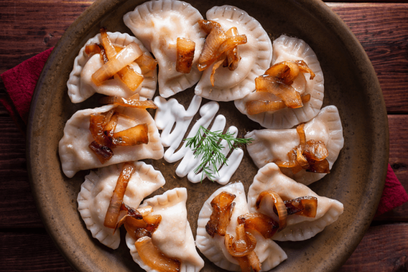 A plate of pierogies with caramelized onions and sour cream.