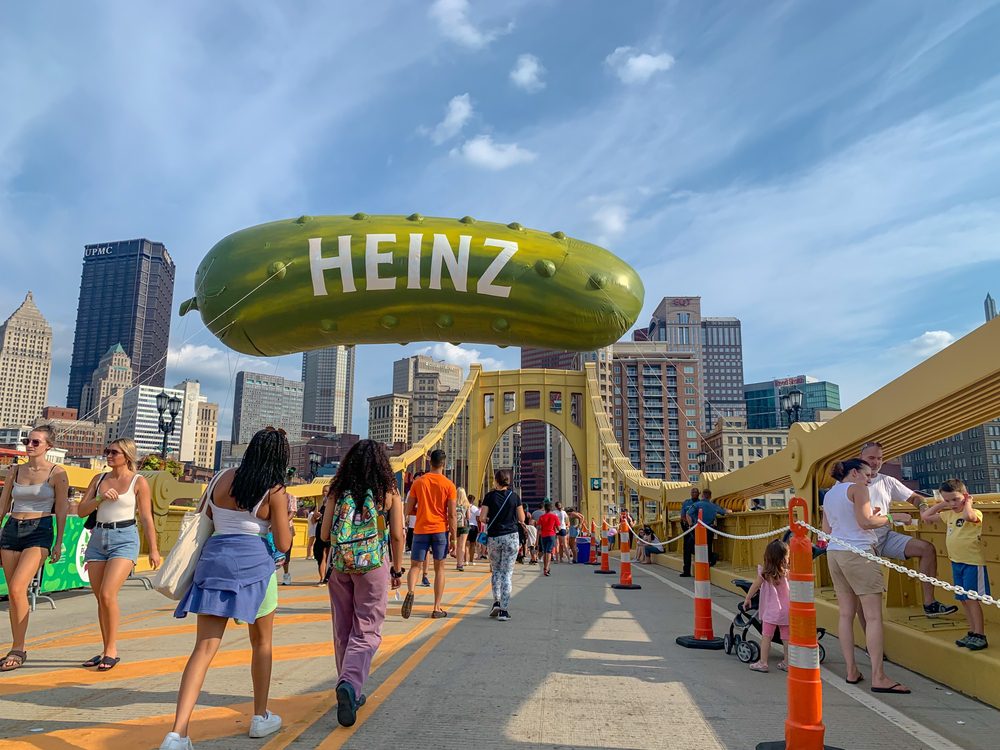 People walking on Andy Warhol Bridge with giant Heinz pickle balloon in the background.