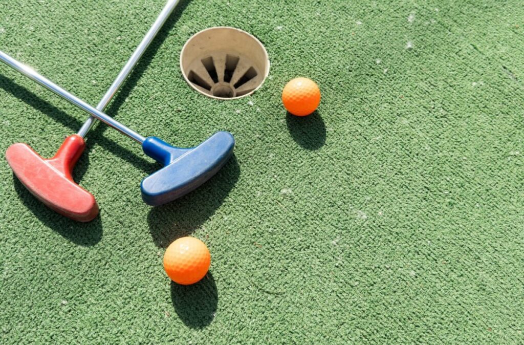 Mini-golf clubs and balls of different colors laid on artificial grass.