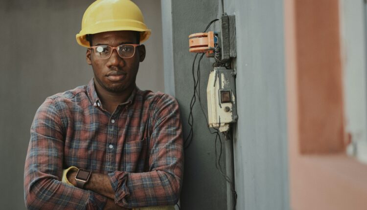 Black construction worker leaning against the wall.