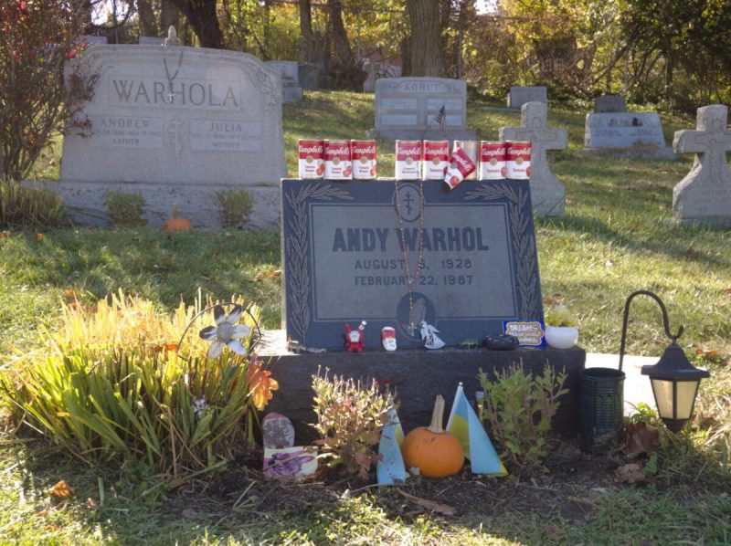the gravesite of artist andy warhol, decorated with cans of soup, pumpkins, and other trinkets.